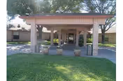 Covered entrance with brick columns leads into the facility, surrounded by green lawn and trees.