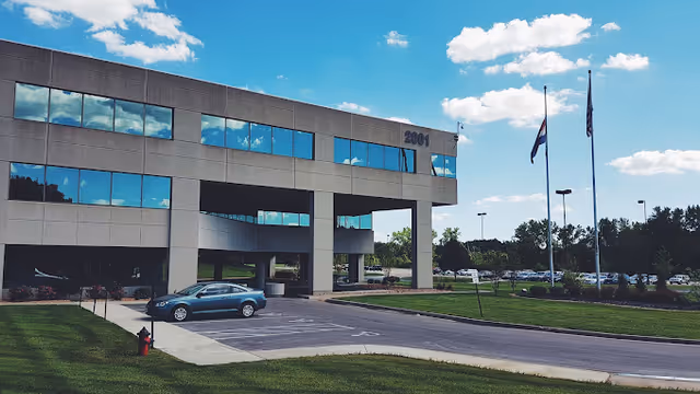Exterior view of a modern two-story medical building facade with glass windows and a parking lot.