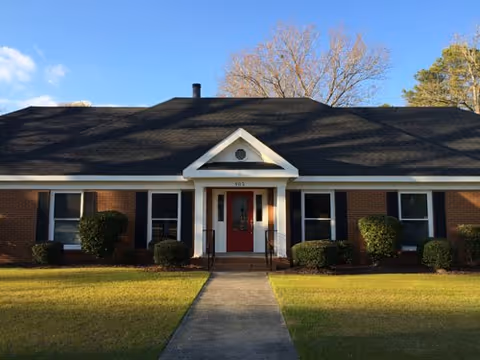 Single-story brick senior care building with red front door and manicured shrubs.