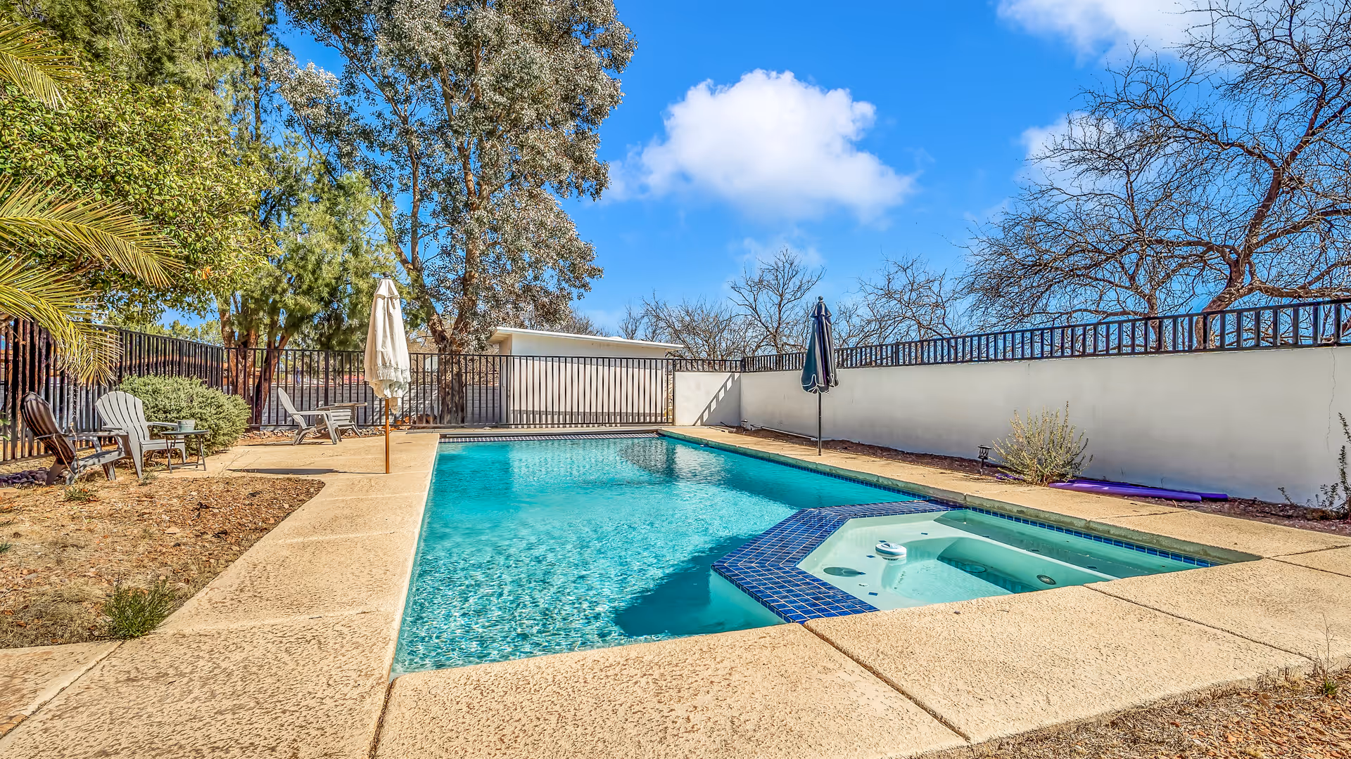Outdoor pool and hot tub area with patio furniture and trees.