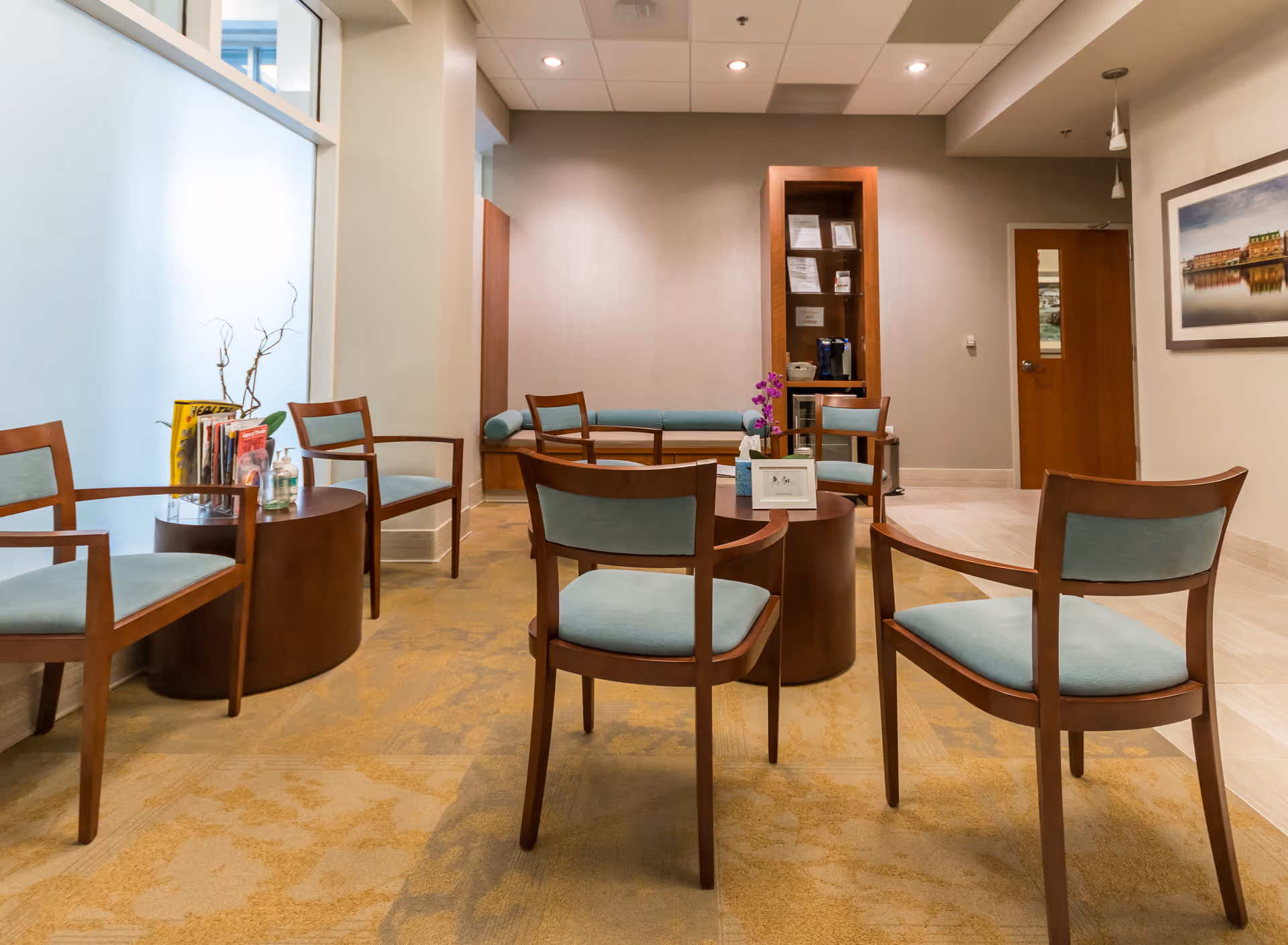 A modern waiting area with wooden chairs around circular tables in a lobby
