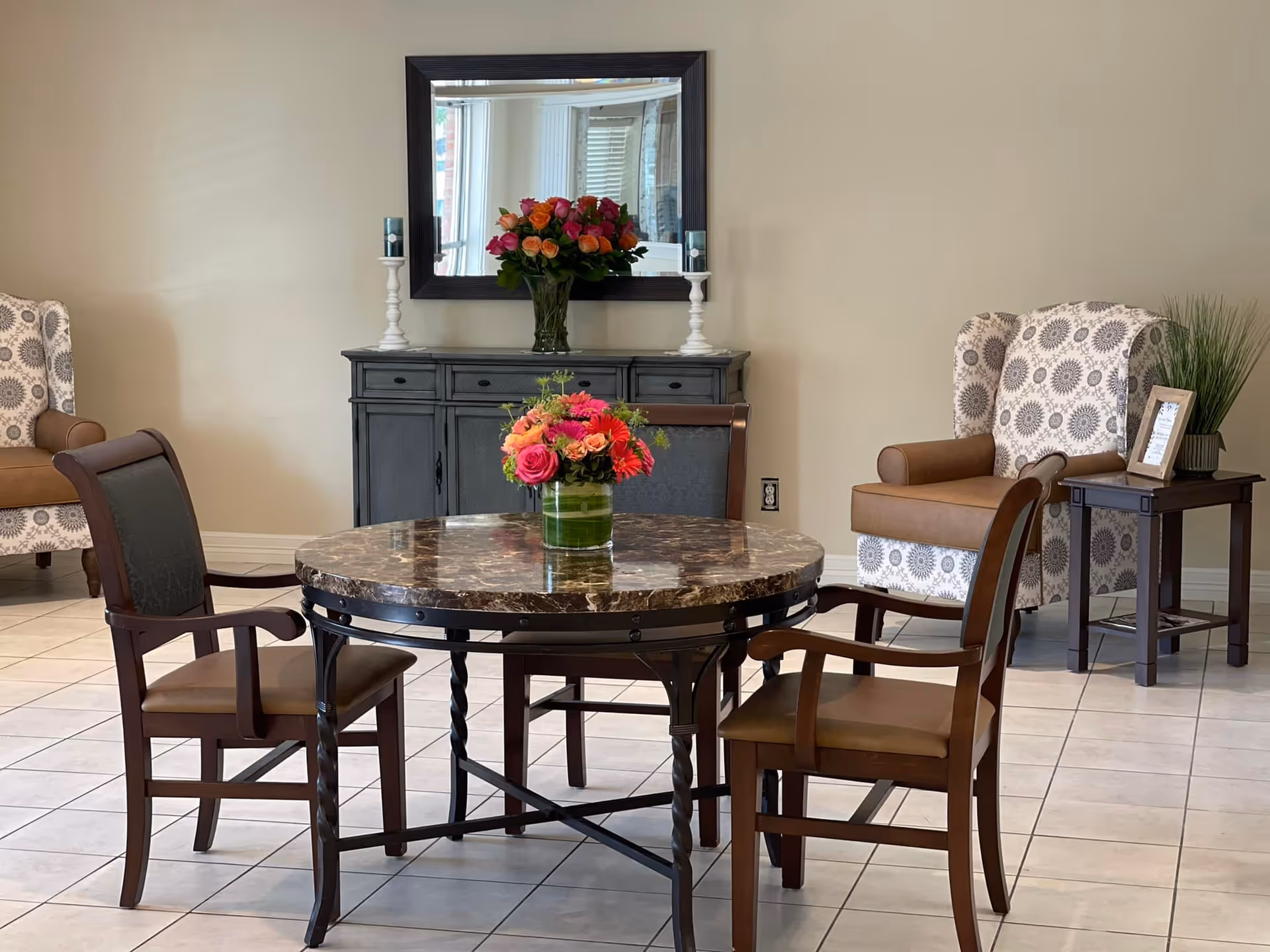 A furnished senior living common area with a round marble table and floral centerpiece.