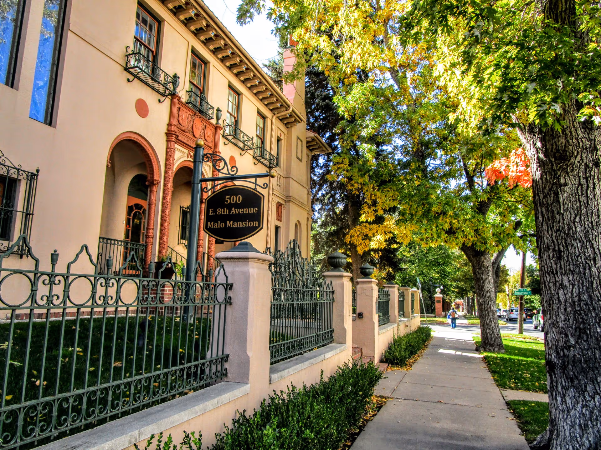 Pastel building exterior with decorative wrought-iron fence and tree-lined sidewalk.