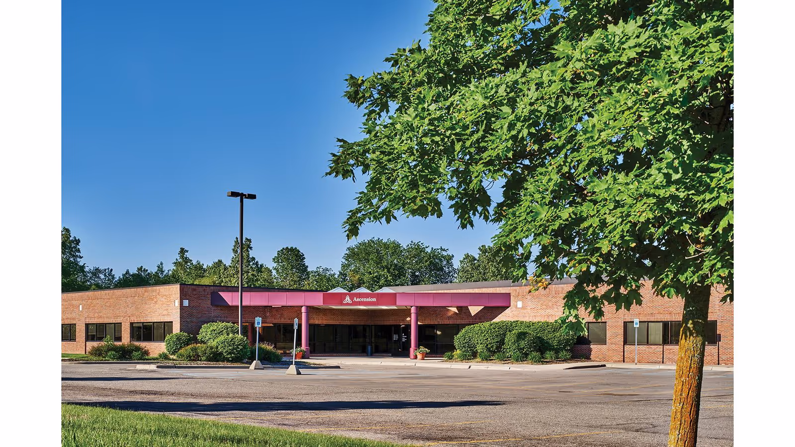 Exterior view of a brick facility entrance with a burgundy canopy and surrounding greenery.