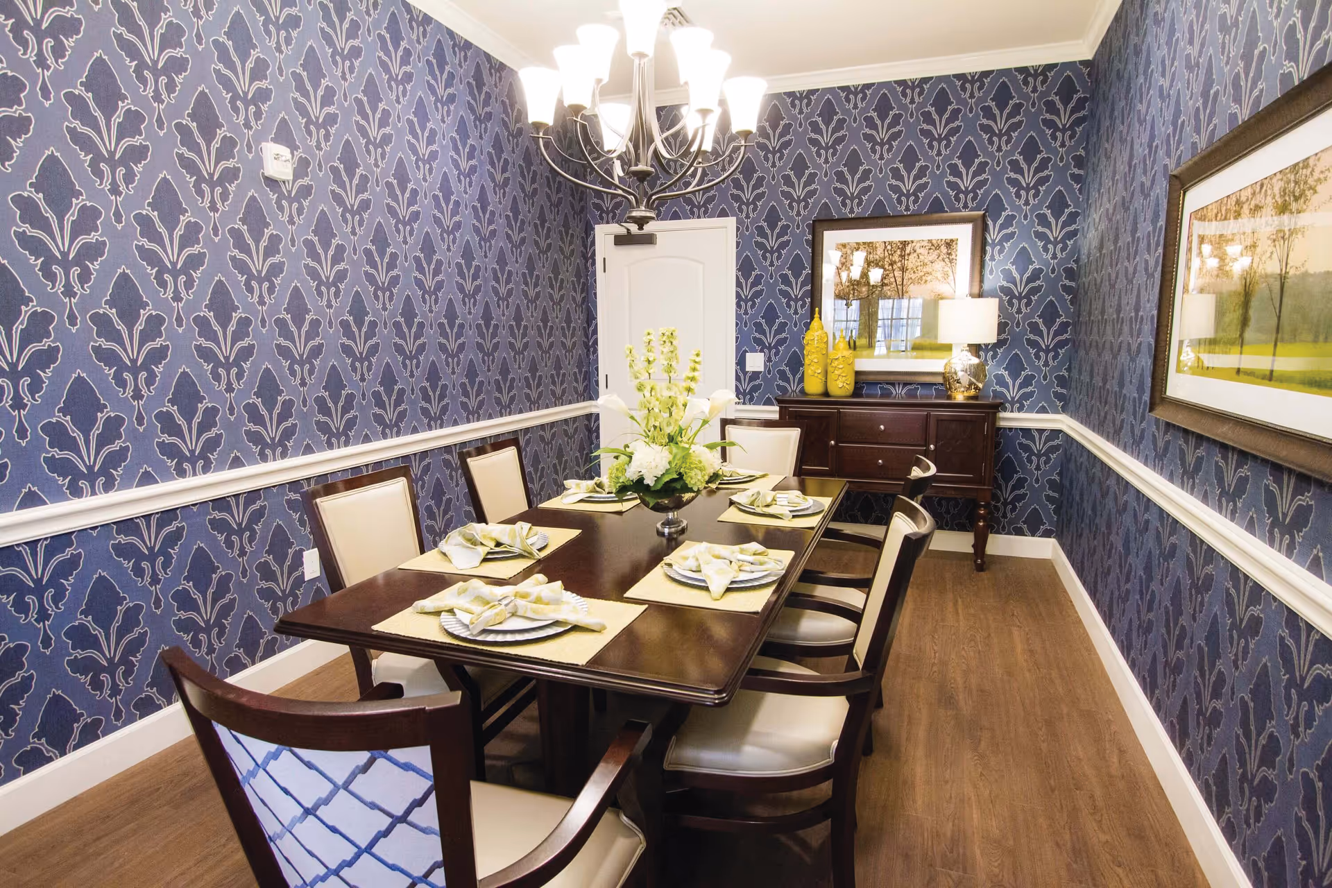 Formal dining room at Liana of Sarasota featuring a long table, chandelier, and blue wallpaper.