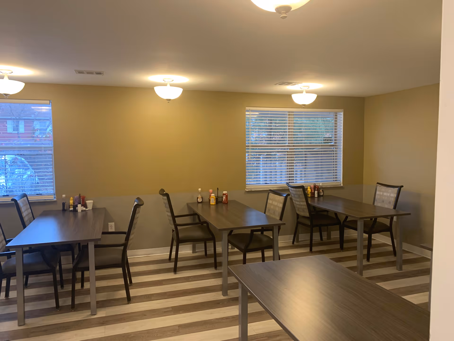 An empty dining room with several tables, chairs, condiments, and striped flooring.