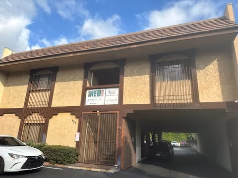 Beige two-story building with a gated entrance and a parked car nearby.