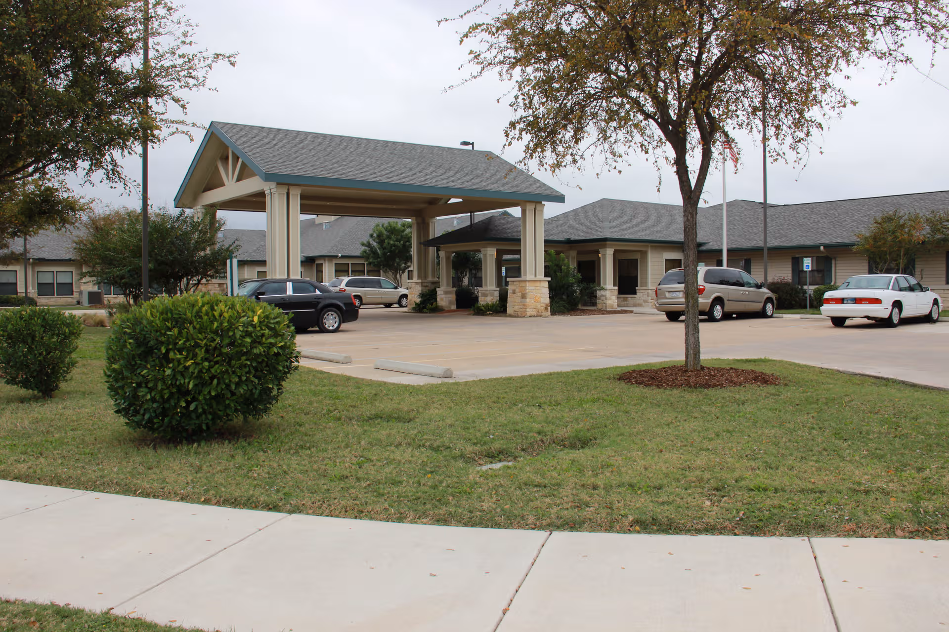 Exterior view of a senior living facility with a covered entrance and parked cars.