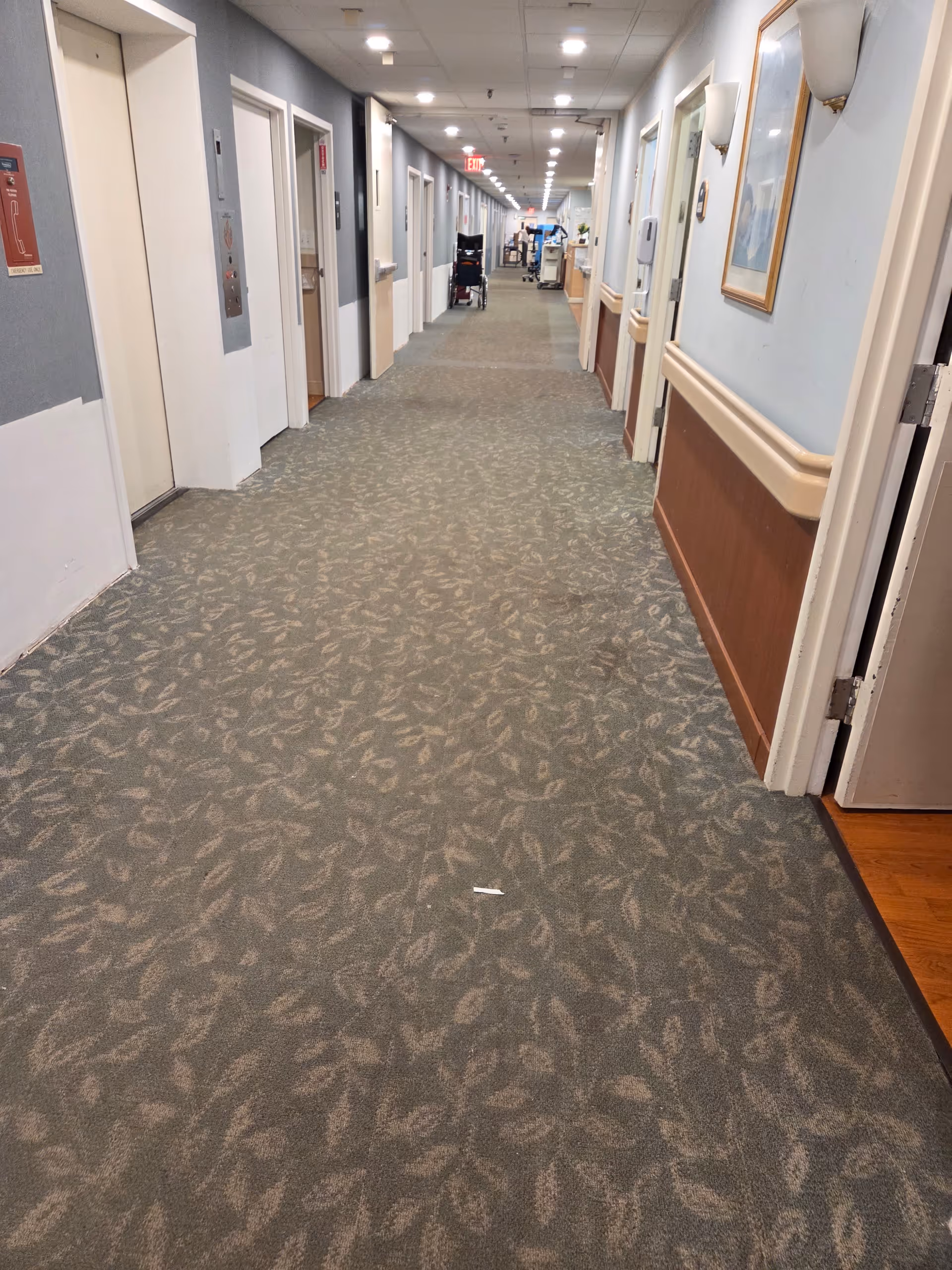 Long interior hallway of a senior living facility with doors on both sides.
