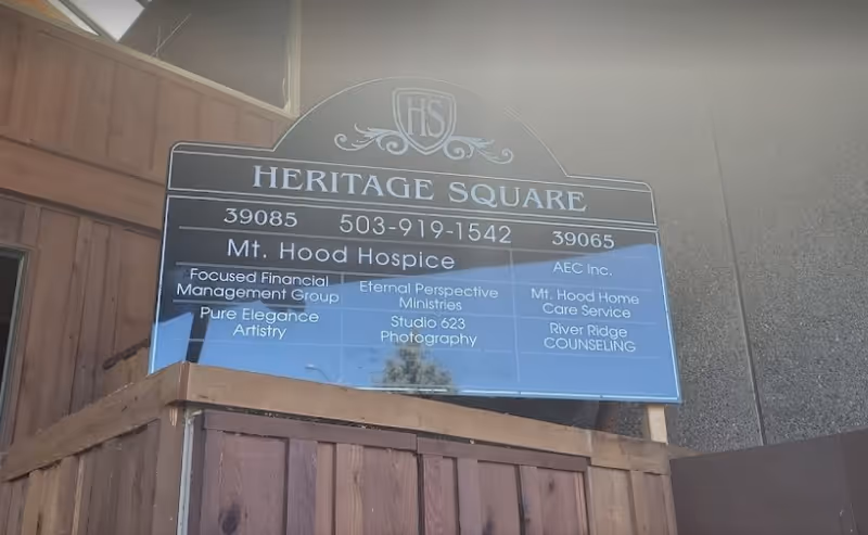 Exterior signboard for Heritage Square featuring Mt. Hood Hospice on a wooden fence.
