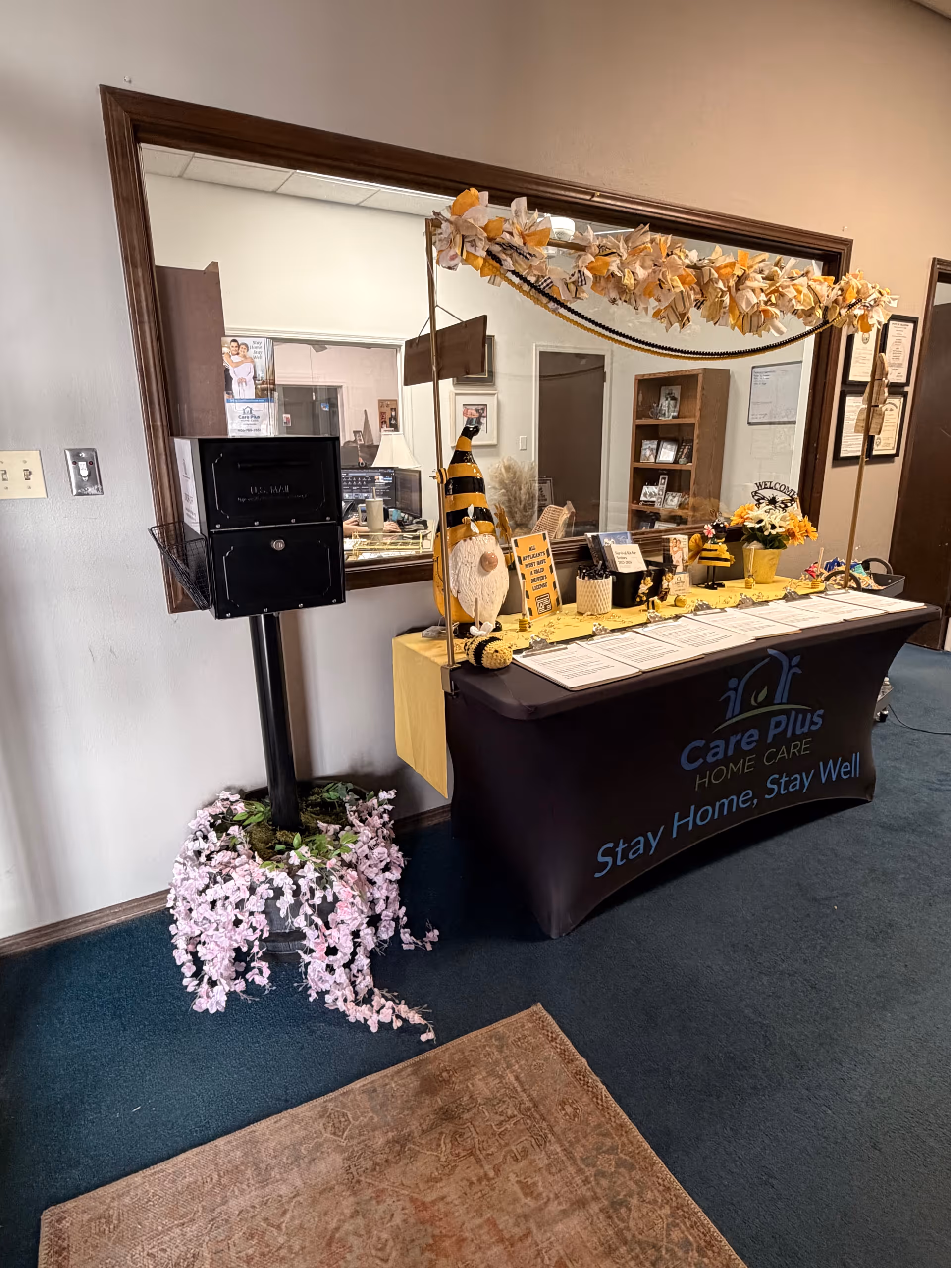 Indoor reception area with a Care Plus Home Care desk, garland decorations, and a large mirror.