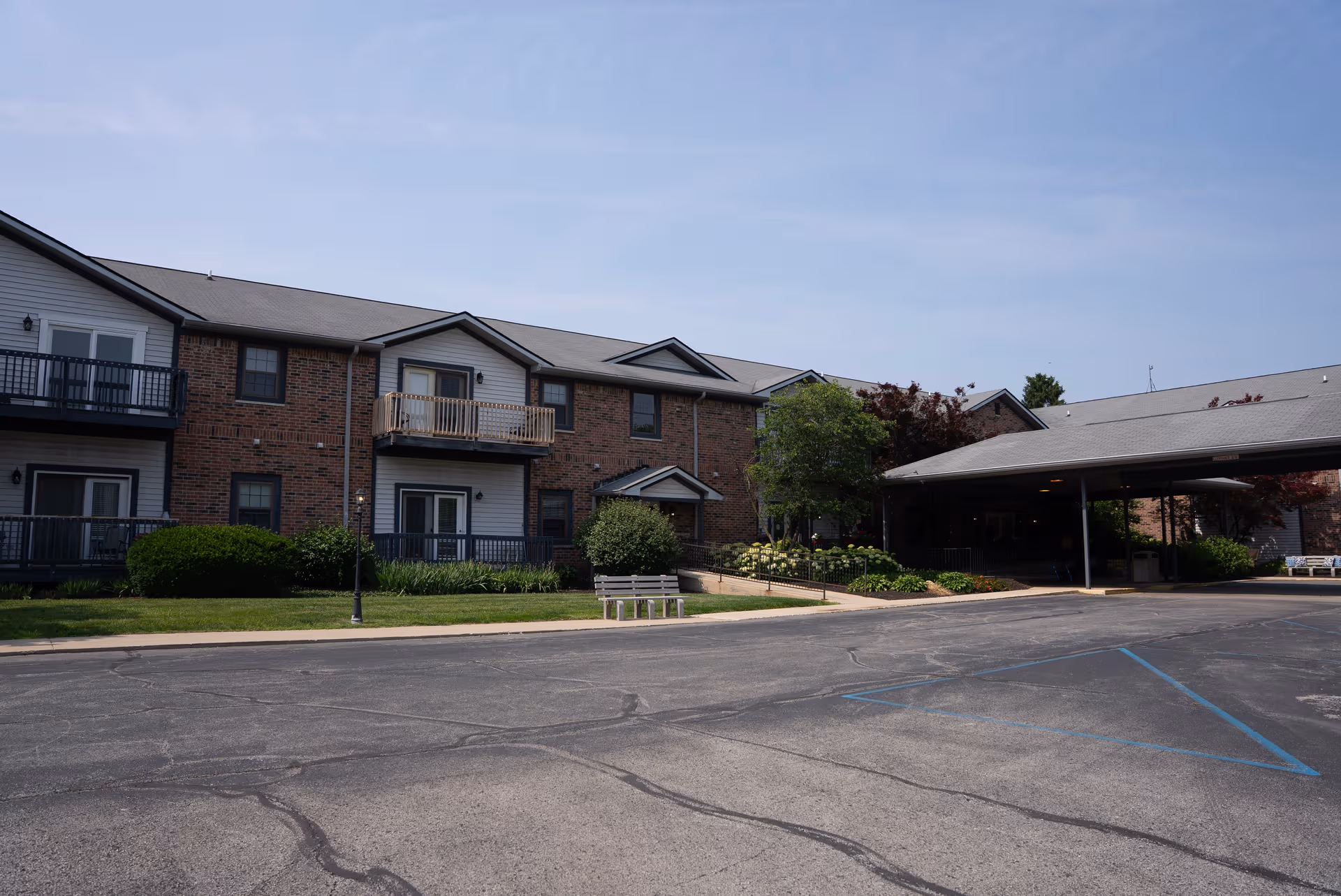 Exterior view of a brick senior living building with a covered entrance and parking lot.