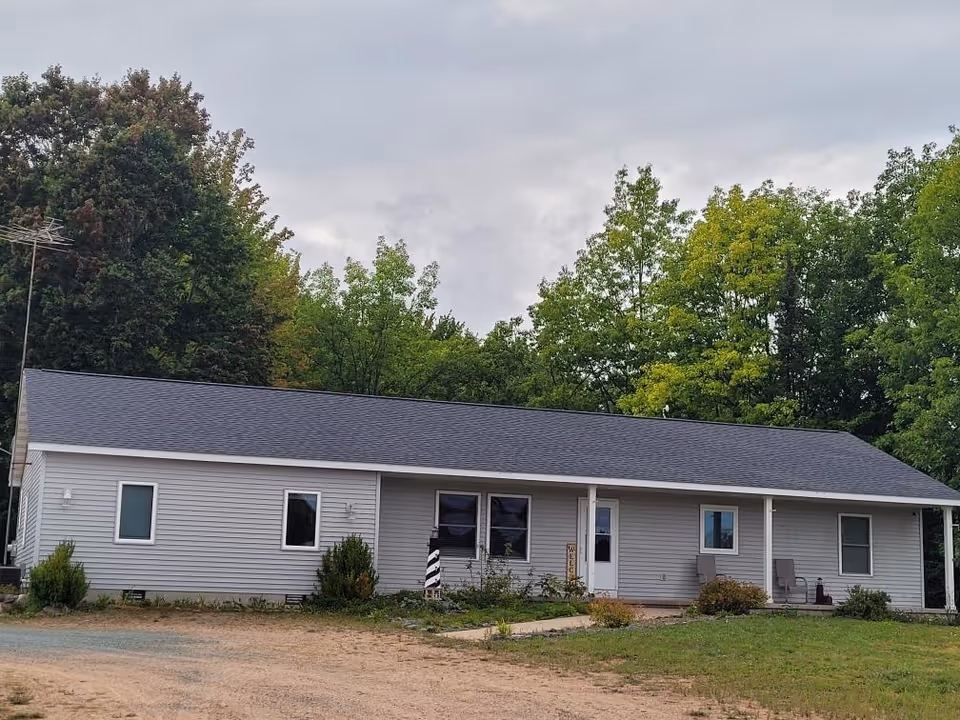 Single story assisted living facility with gray siding, front porch seating, and trees.
