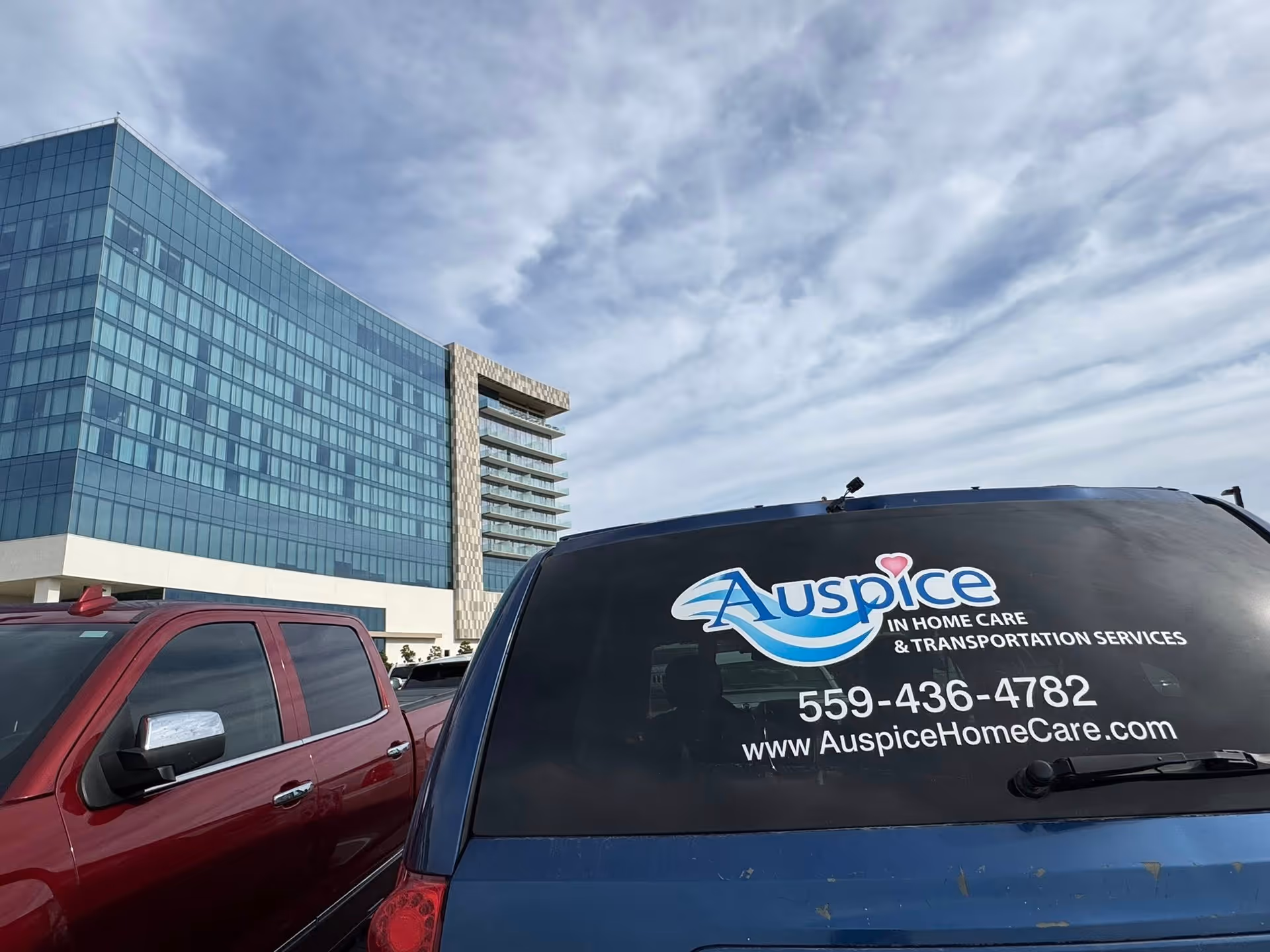 Blue Auspice van with logo parked beside a modern glass building.
