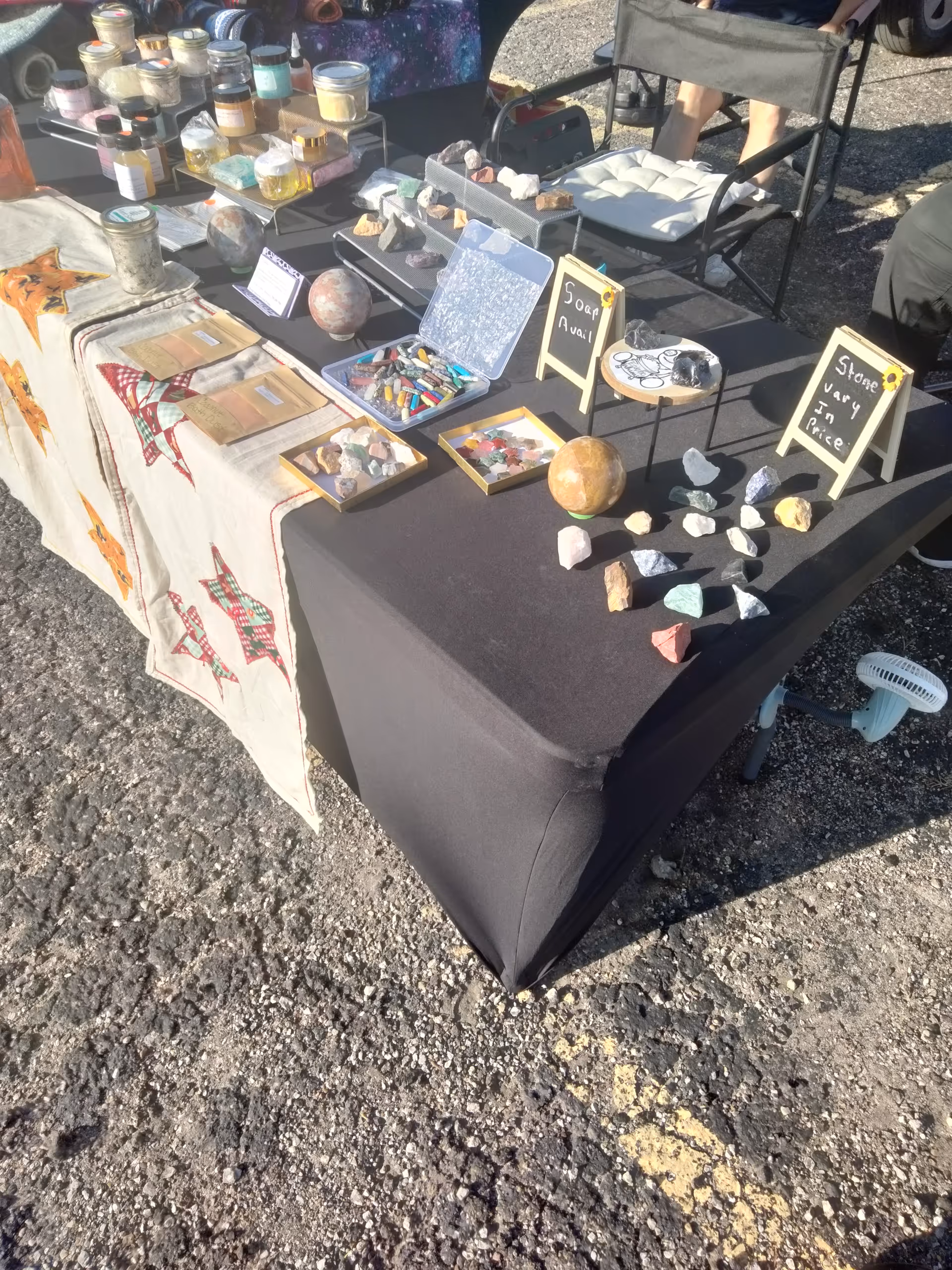 Outdoor vendor table with a black cloth displaying rocks, crystals, soaps, and small crafts.