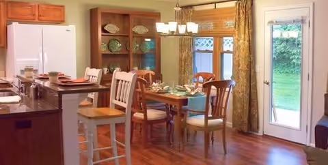 Open dining area with a wooden table, chairs, chandelier, hutch, and glass door to outside.