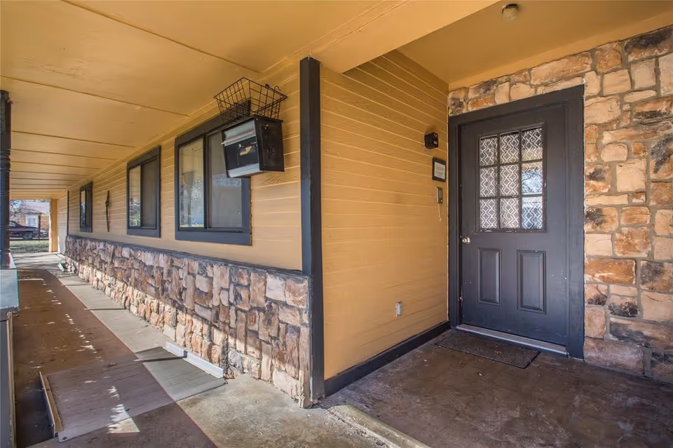 Covered exterior entryway with a stone-faced lower wall, a row of windows, and a dark front door.
