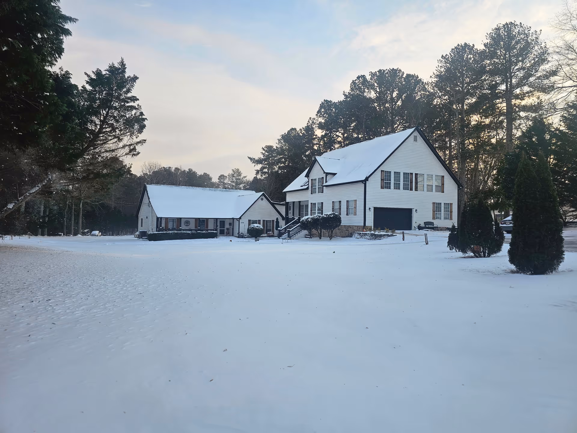 Snow-covered white senior living facility exterior with multiple buildings and tall trees.