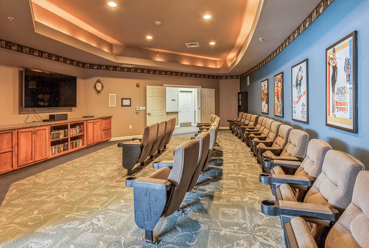 Interior lounge in a senior living facility with theater seating and posters.