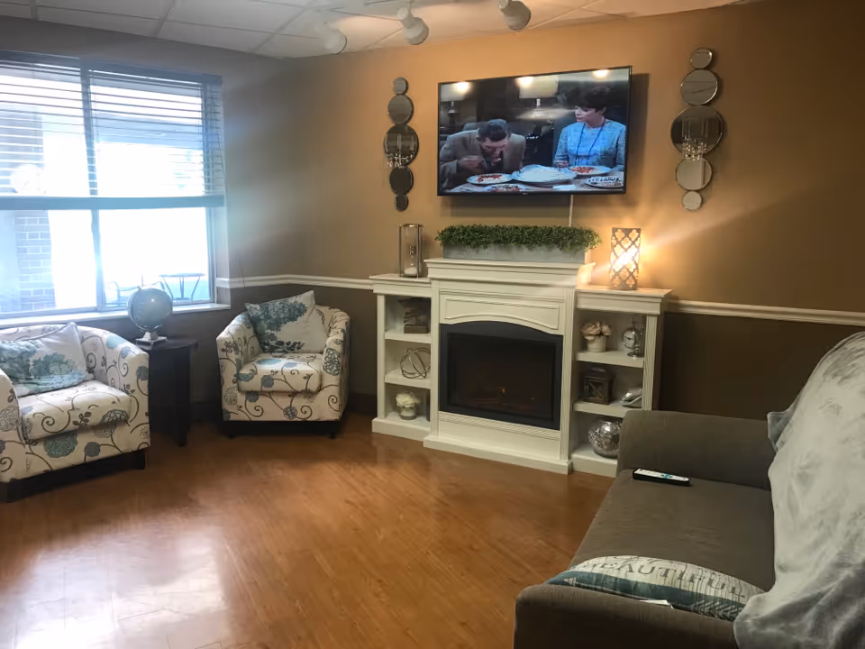 Cozy living area with patterned chairs, sofa, fireplace, and mounted TV.