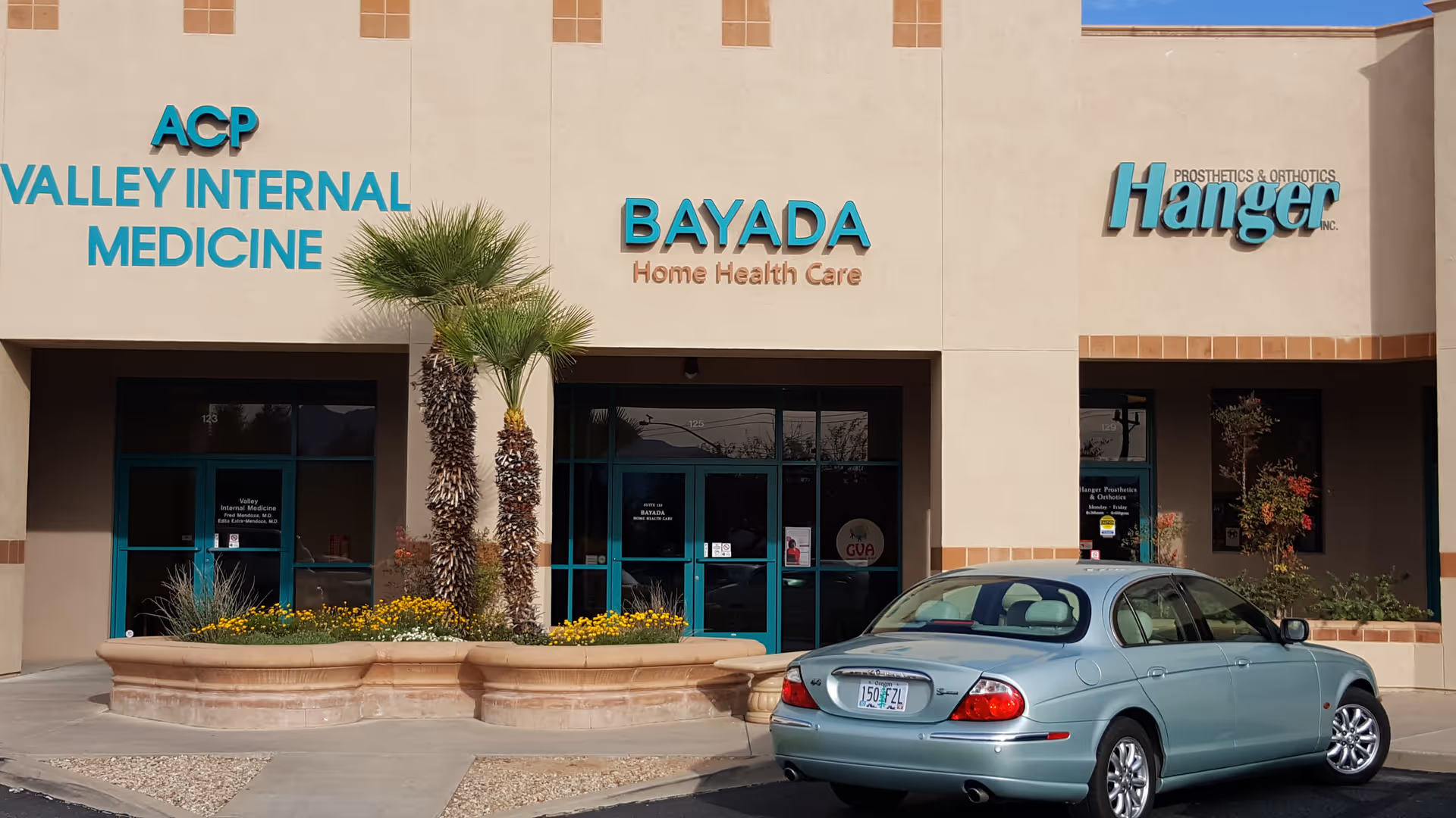Beige medical building facade with BAYADA sign, palm trees, planters, and a parked car.