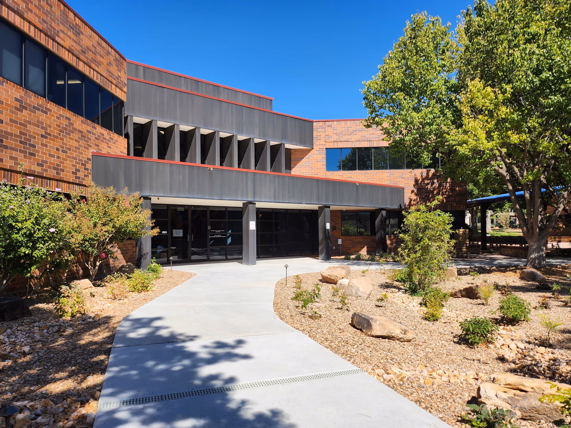 Inteli-Care LLC facility exterior with glass entry, brick facade, concrete walkway, and drought-tolerant landscaping.