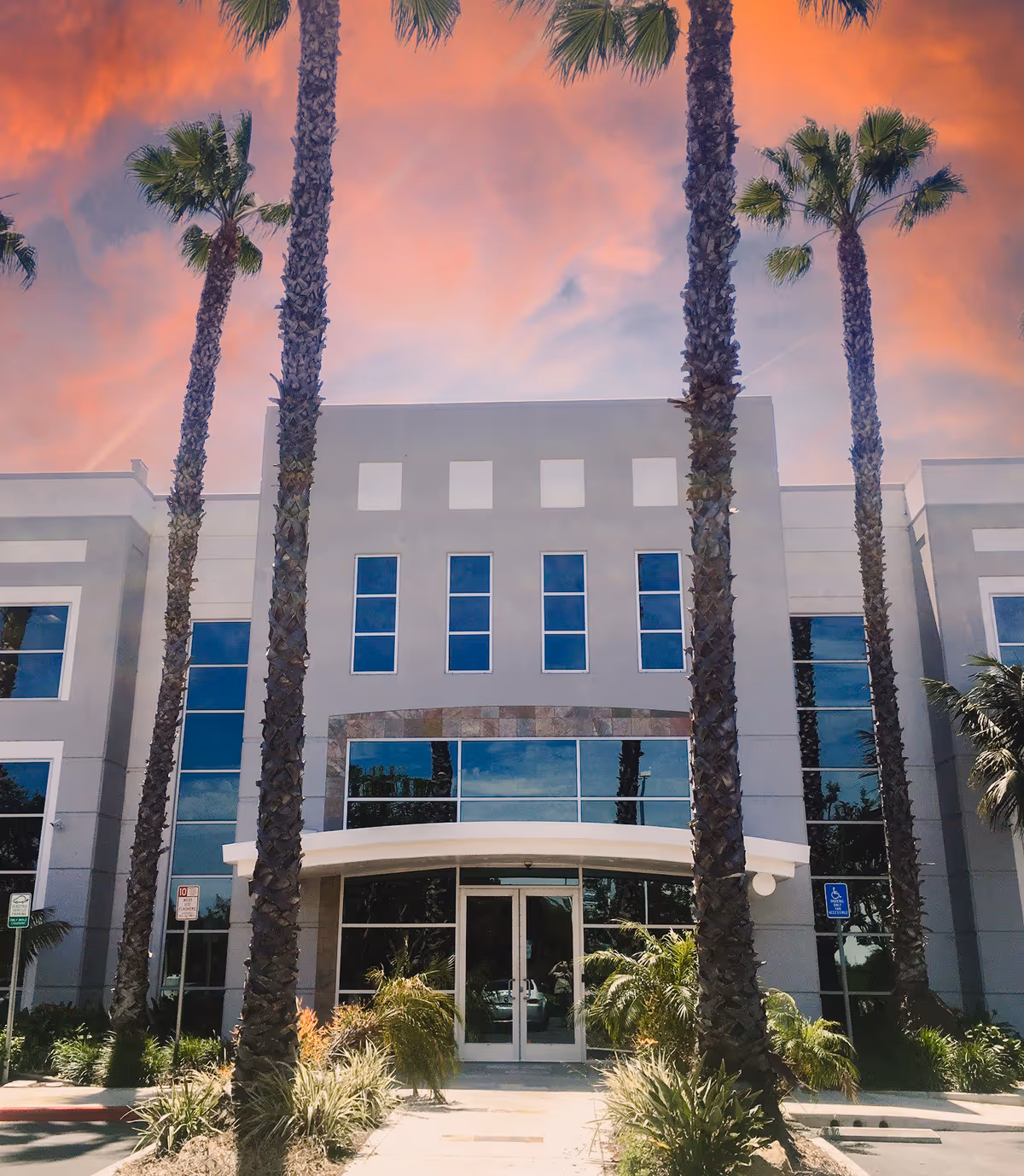 Modern senior living facility entrance with tall palm trees and a glass-front facade.