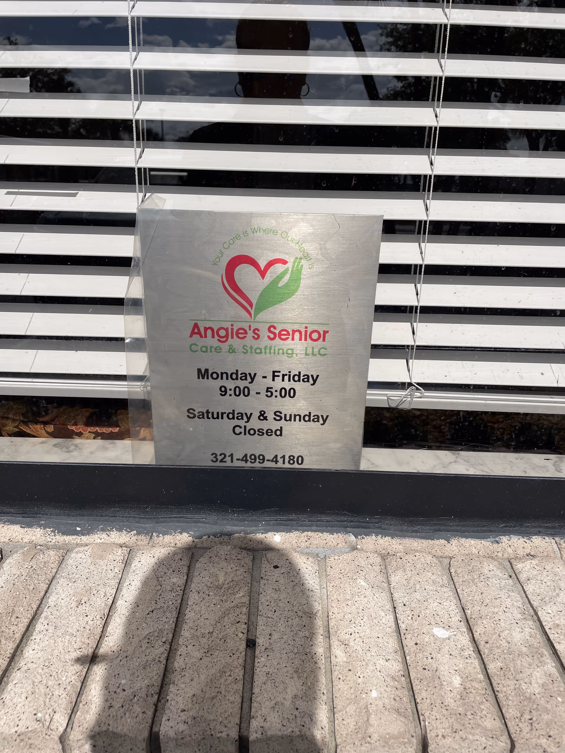 Metal sign for Angie's Senior Care & Staffing sits outside striped storefront window.
