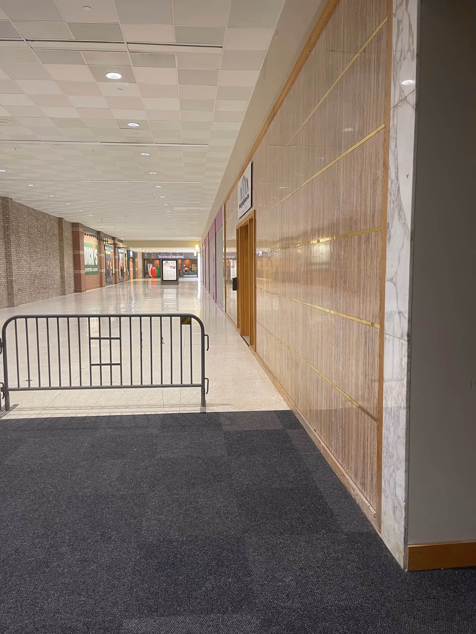 Long indoor corridor in a senior living facility with storefronts and a metal barrier.