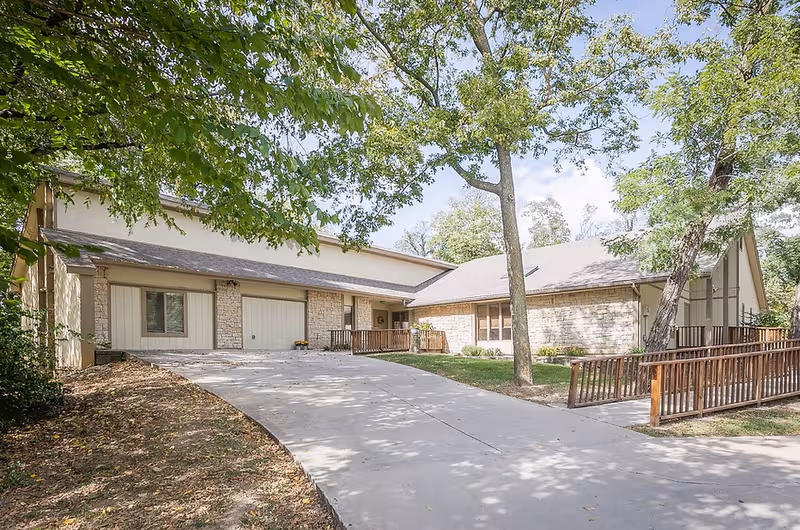 Front view of a senior living facility with driveway, garages, and trees.