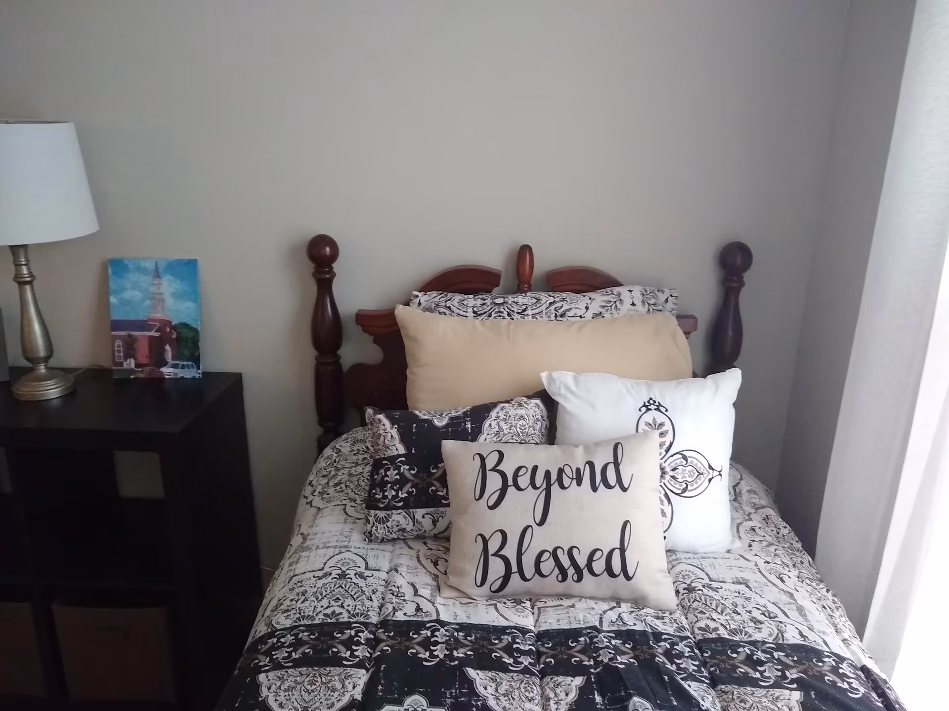 Cozy bedroom with patterned bedspread, decorative pillows, nightstand, and a lamp.