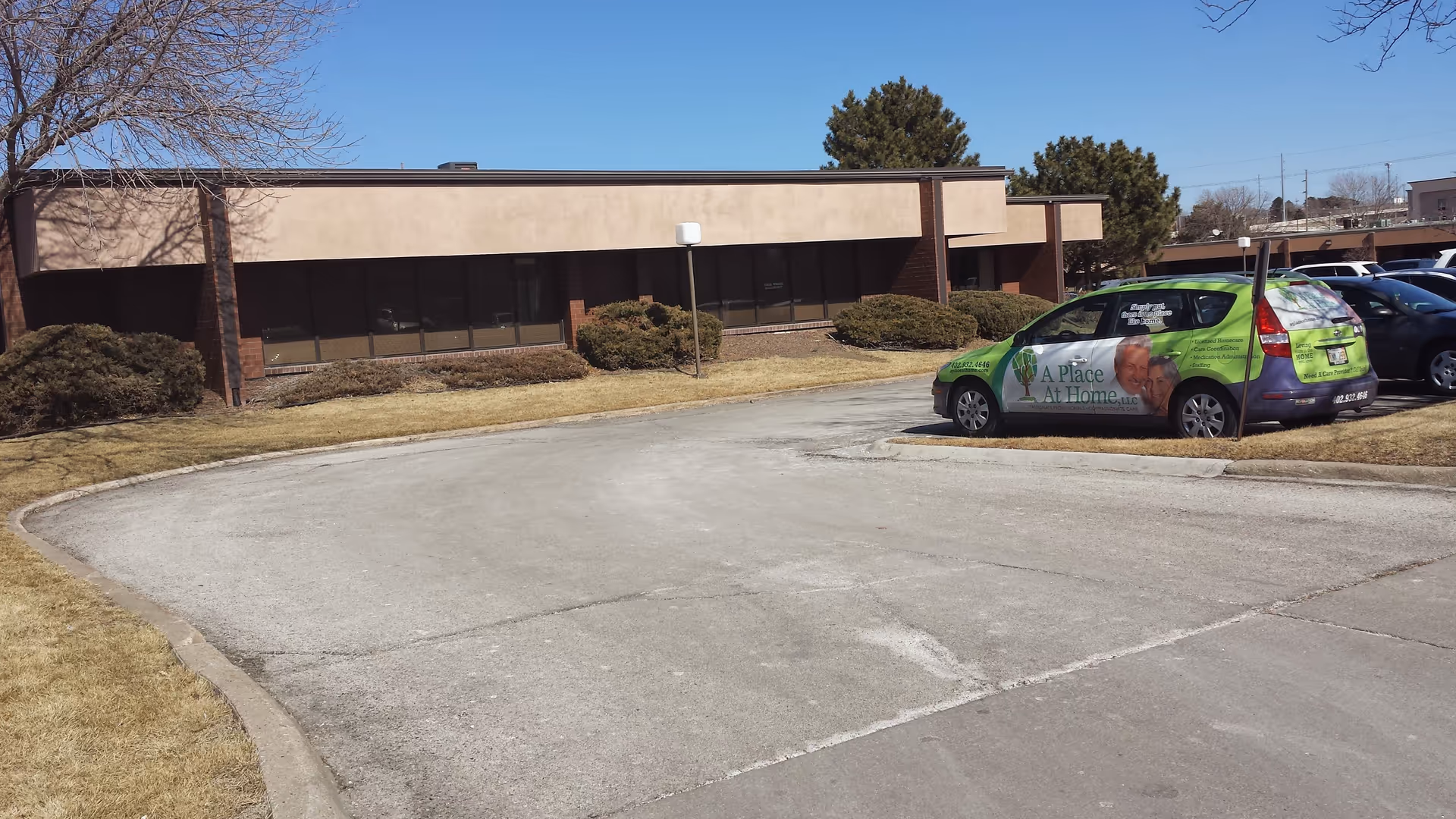 Exterior view of a low, brick senior facility with a green A Place At Home van.