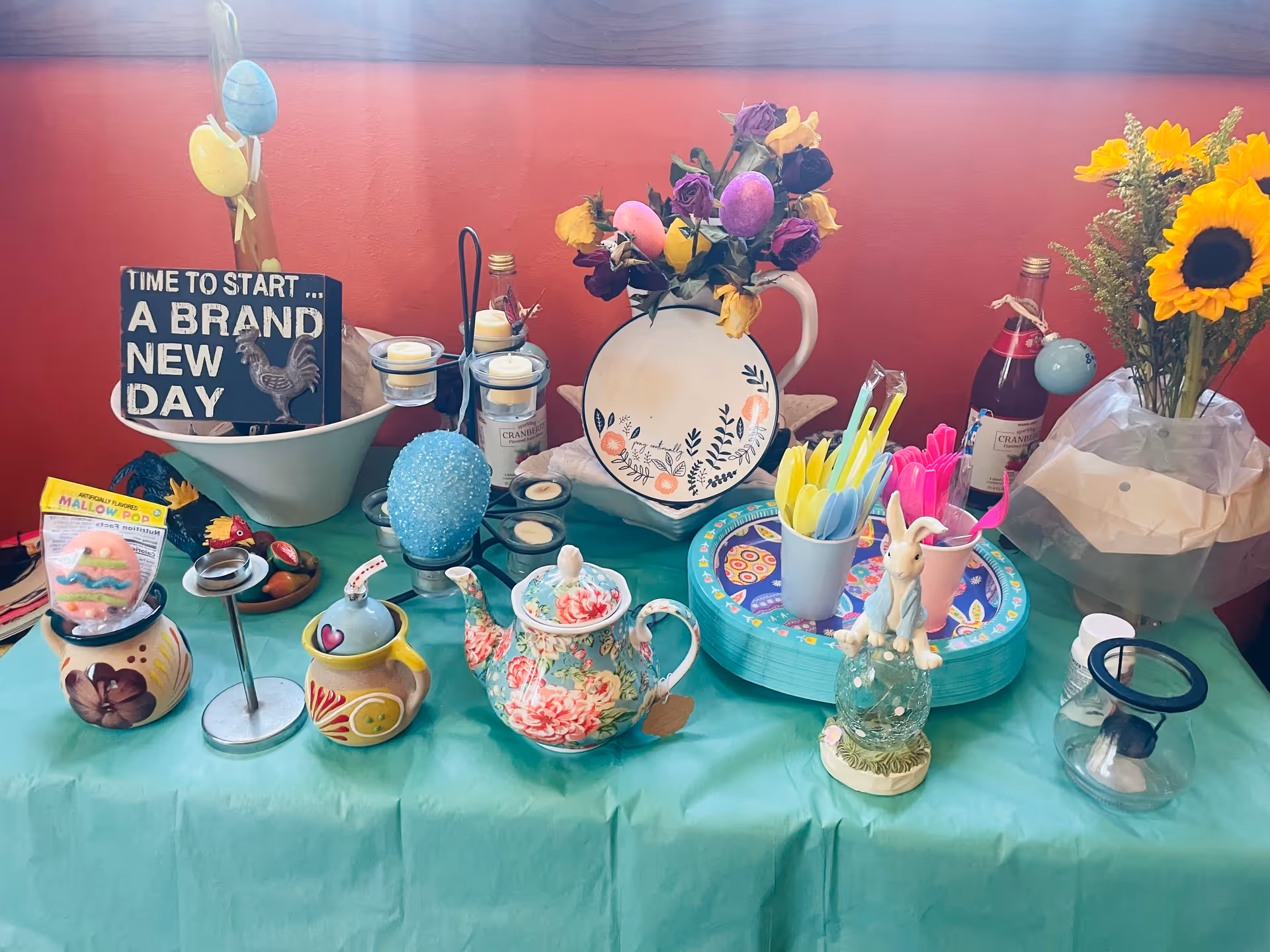 Colorful table decor with teapots, flowers, and Easter items on a teal tablecloth.