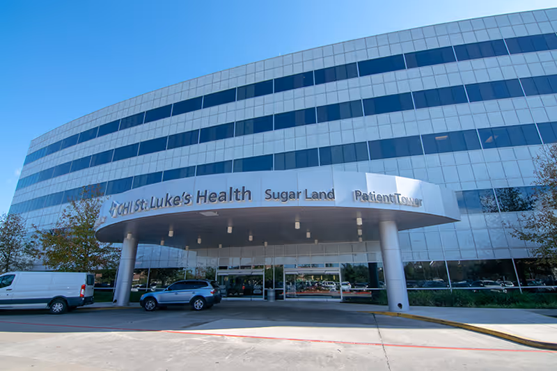 Modern glass-front medical building with curved entrance canopy and vehicles parked outside.