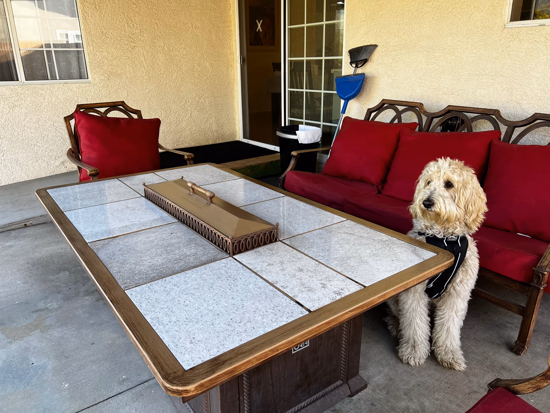 Outdoor patio with red-cushioned seating, a tiled table, and a dog beside the door.