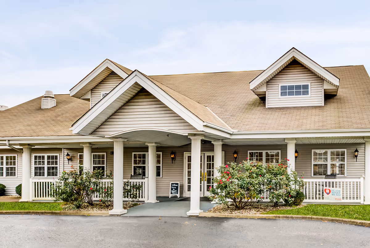 Senior living facility building exterior with a covered porch, columns, and flowering shrubs.