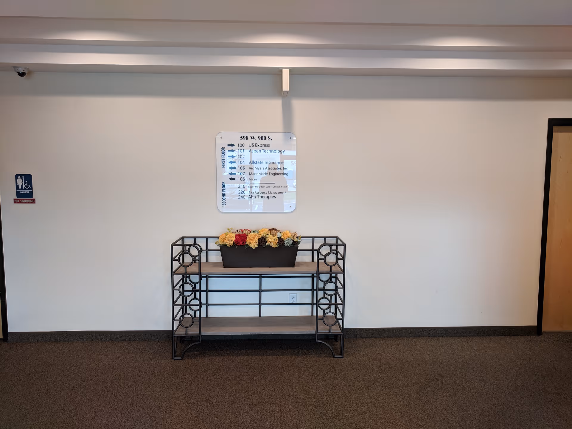 Interior hallway with a metal console table, flower arrangement, and directory sign on beige wall.