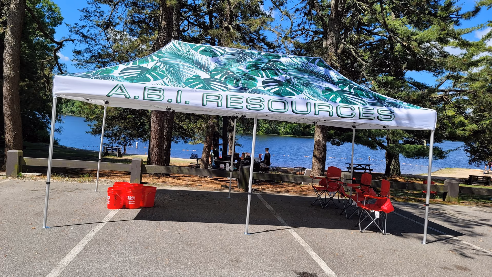 An A.B.I. Resources tent set up outdoors by a lake with red chairs.