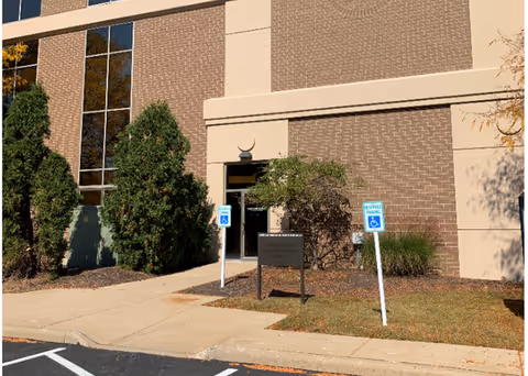 Exterior view of a brick building entrance with handicapped parking signs and landscaping.