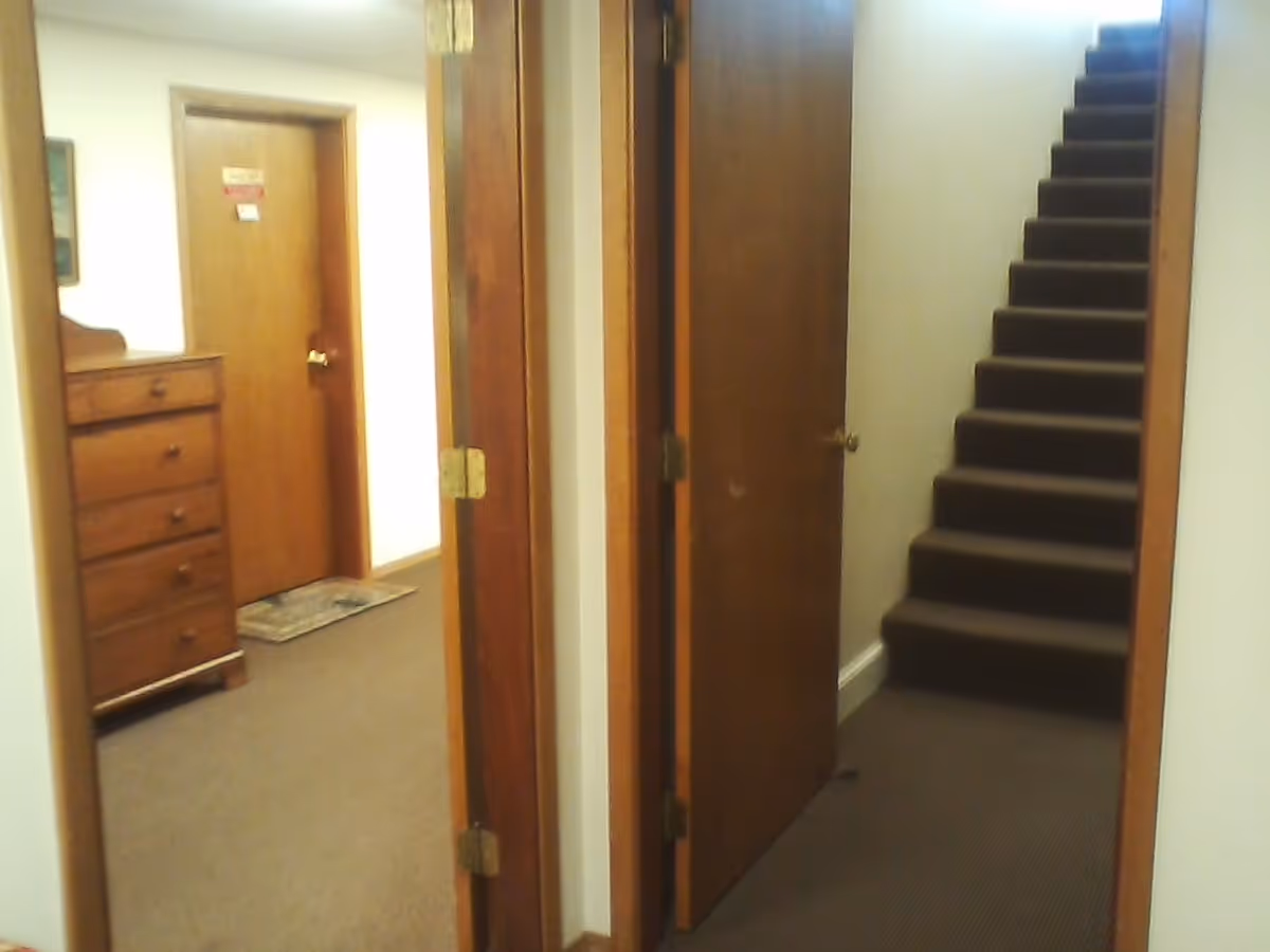 Interior hallway of a senior living facility with open doors and carpeted stairs.