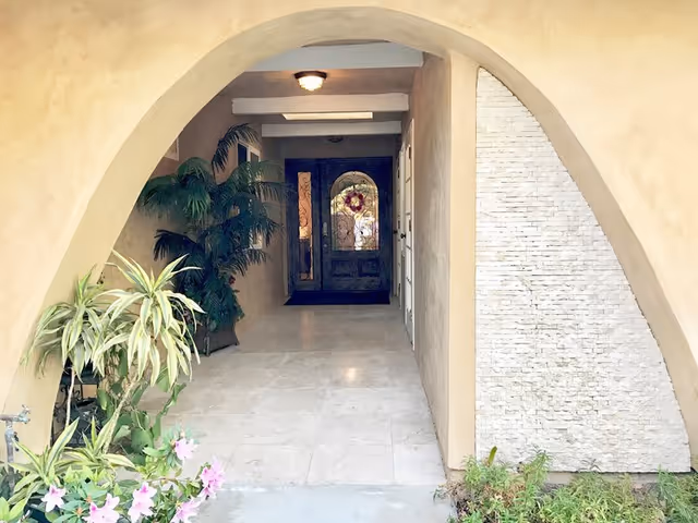 Arched entryway with tiled floor, potted plants, and a dark doorway at the end.