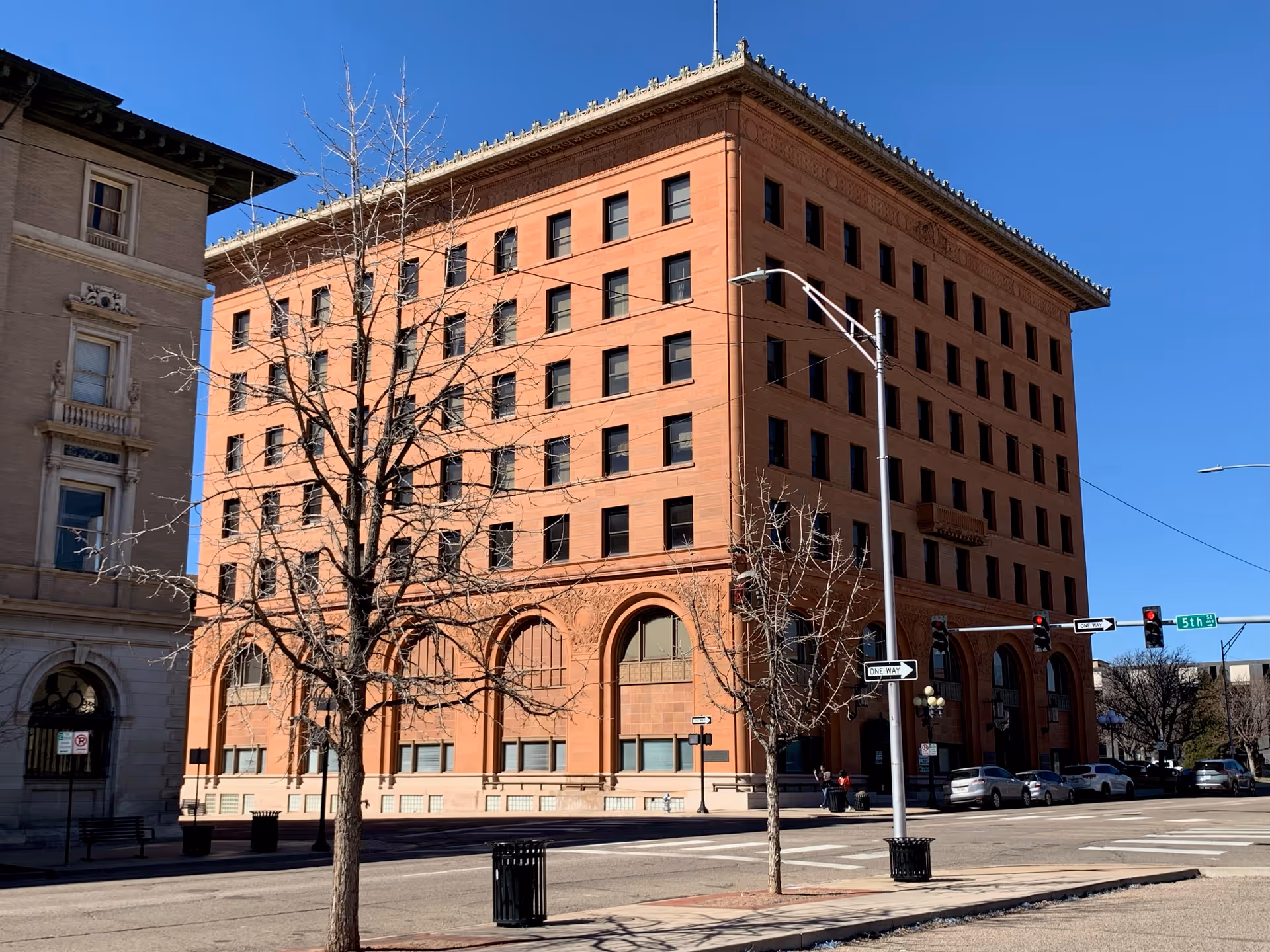 Tall brick multi-story building on a street corner with leafless trees.