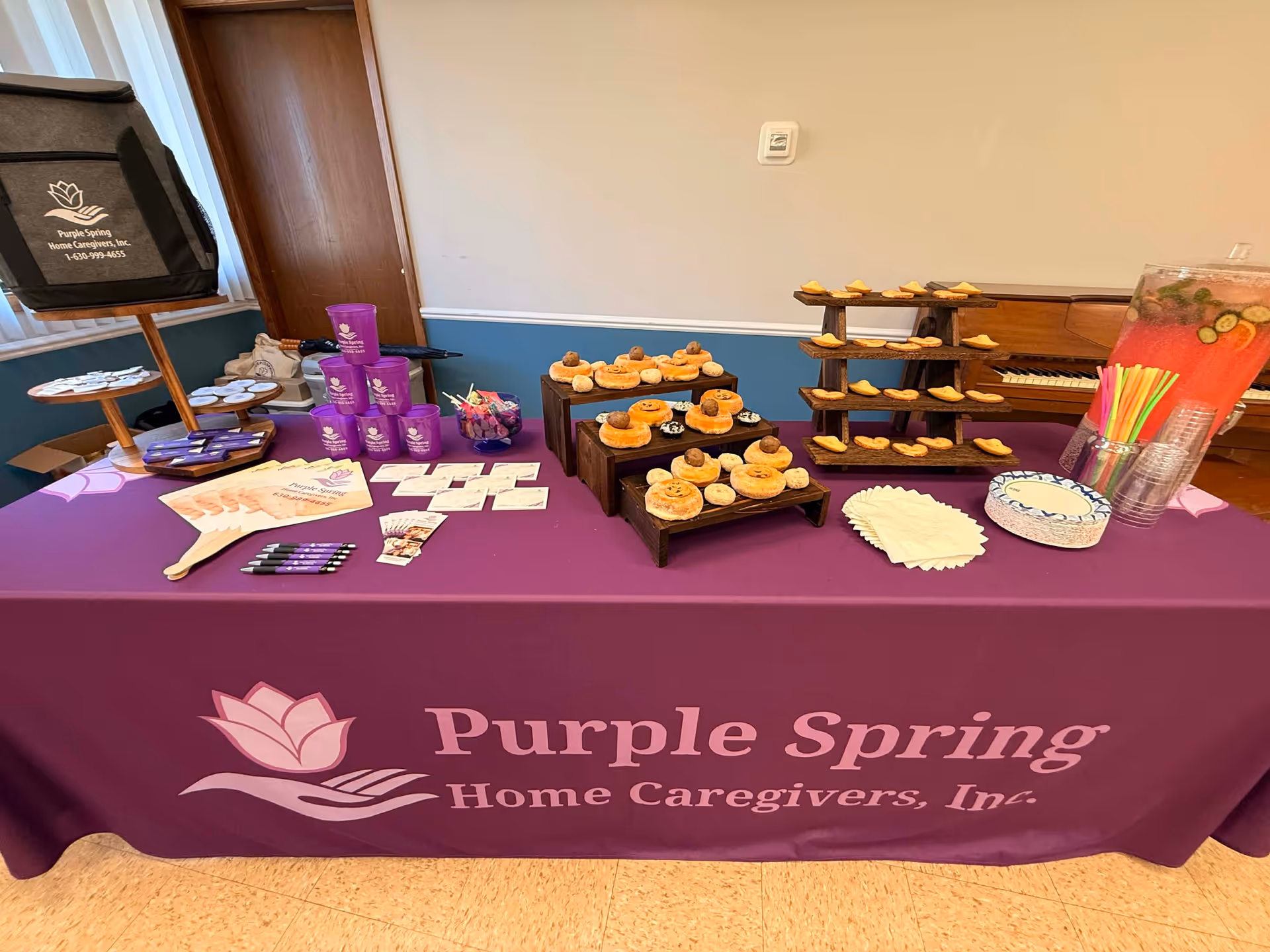 Indoor table display with pastries and cups on a purple tablecloth labeled Purple Spring Home Caregivers.