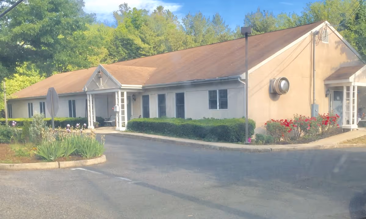 Single-story beige senior living facility with front entrance, hedges, and flowering landscaping.