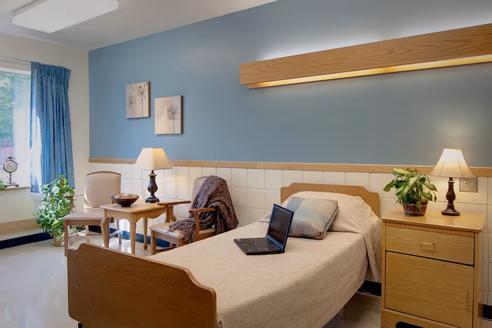 A furnished bedroom in a senior facility with bed, nightstands, and seating area.