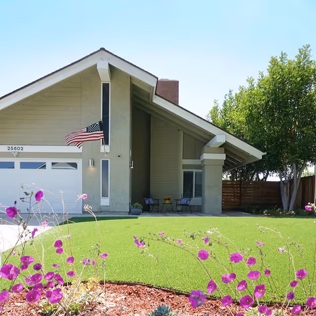 Front exterior of Sacred Heart Senior Care, with a manicured lawn, flowers, and seating.