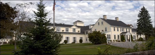 Exterior view of Pond Home, a large white senior living facility with flagpole and manicured lawn.