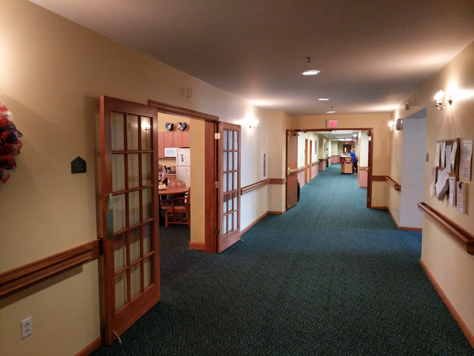 A long hallway in a senior care facility with doors and a distant reception desk.