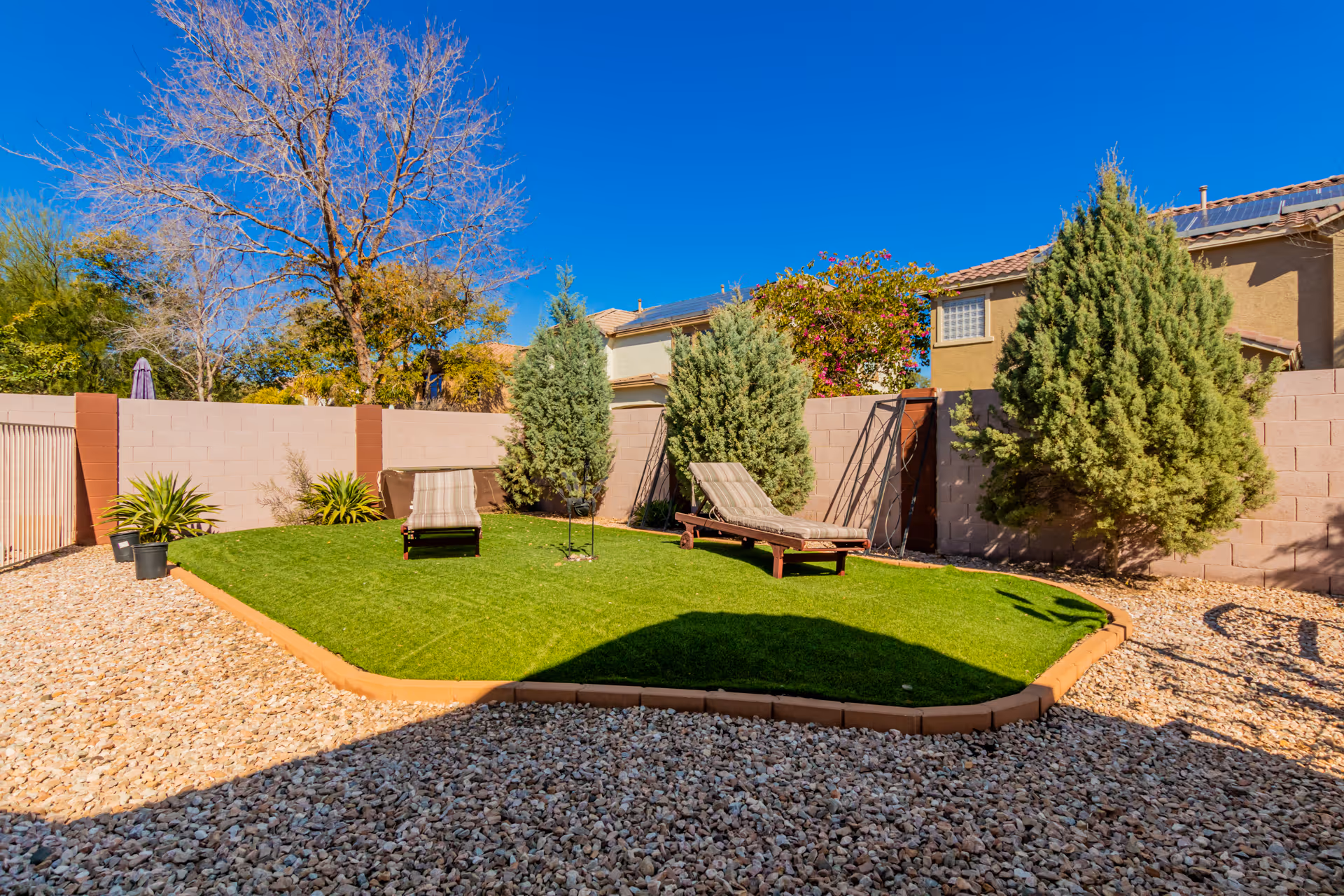 A fenced courtyard with a small grassy area and lounge chairs.