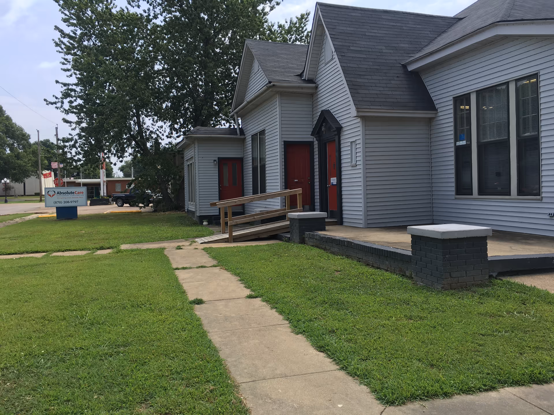 Exterior view of a white facility with red doors, ramp, and sign on lawn.